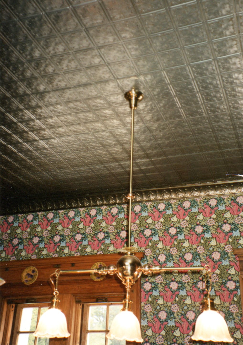 Vintage-style chandelier hanging from a tin ceiling with floral wallpaper.