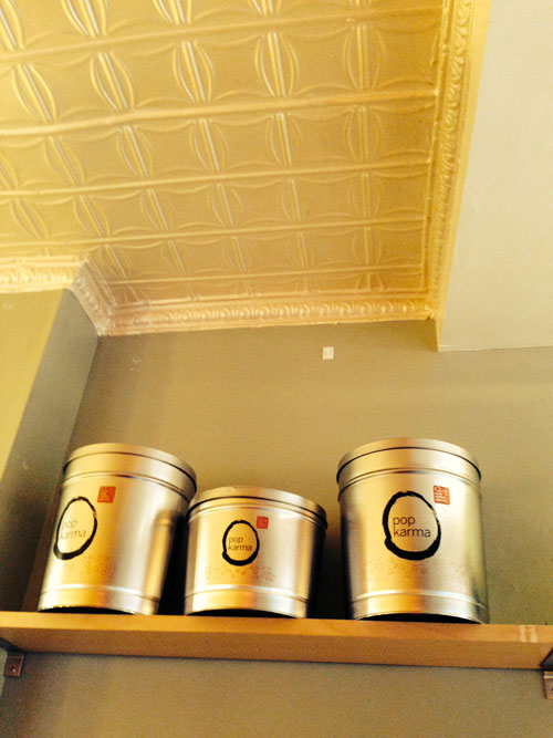 Three silver metal containers with a logo on a shelf against a light-colored wall.