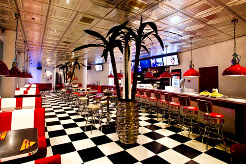 Diner interior with checkered floor, red chairs, and palm tree decorations.
