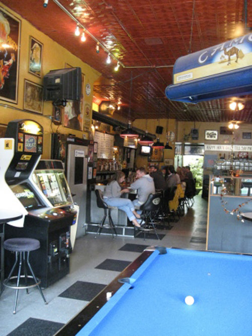 Bar with arcade games, pool table, and people sitting at the bar.