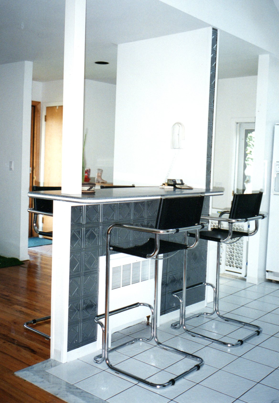 Modern kitchen with a bar area featuring black bar stools and a white countertop.