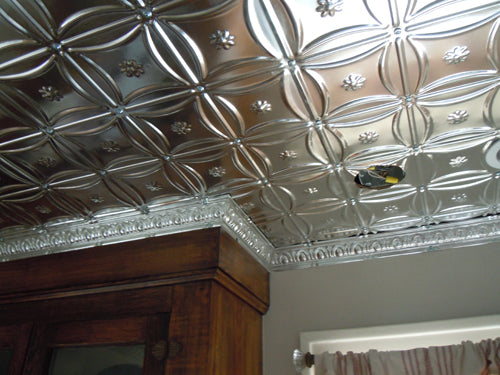 Decorative ceiling with metallic tile pattern and wooden furniture.