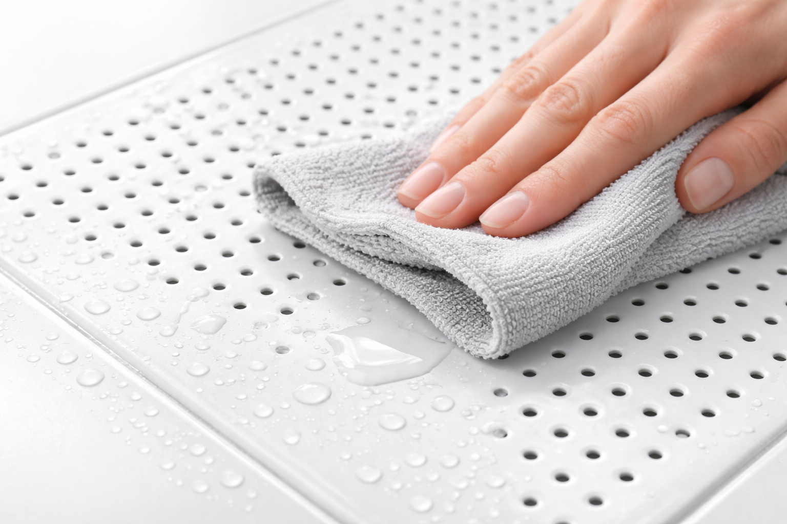 Hand using a gray towel to dry a white perforated mat.