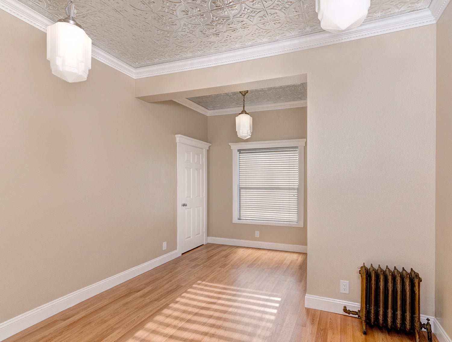 Empty room with beige walls, wooden floor, and decorative ceiling.