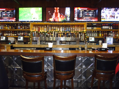 Bar with wooden bar counter, stools, and multiple televisions displaying sports on the wall.