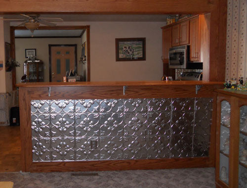 Metallic backsplash with wooden frame in a room with cabinets and a mirror.