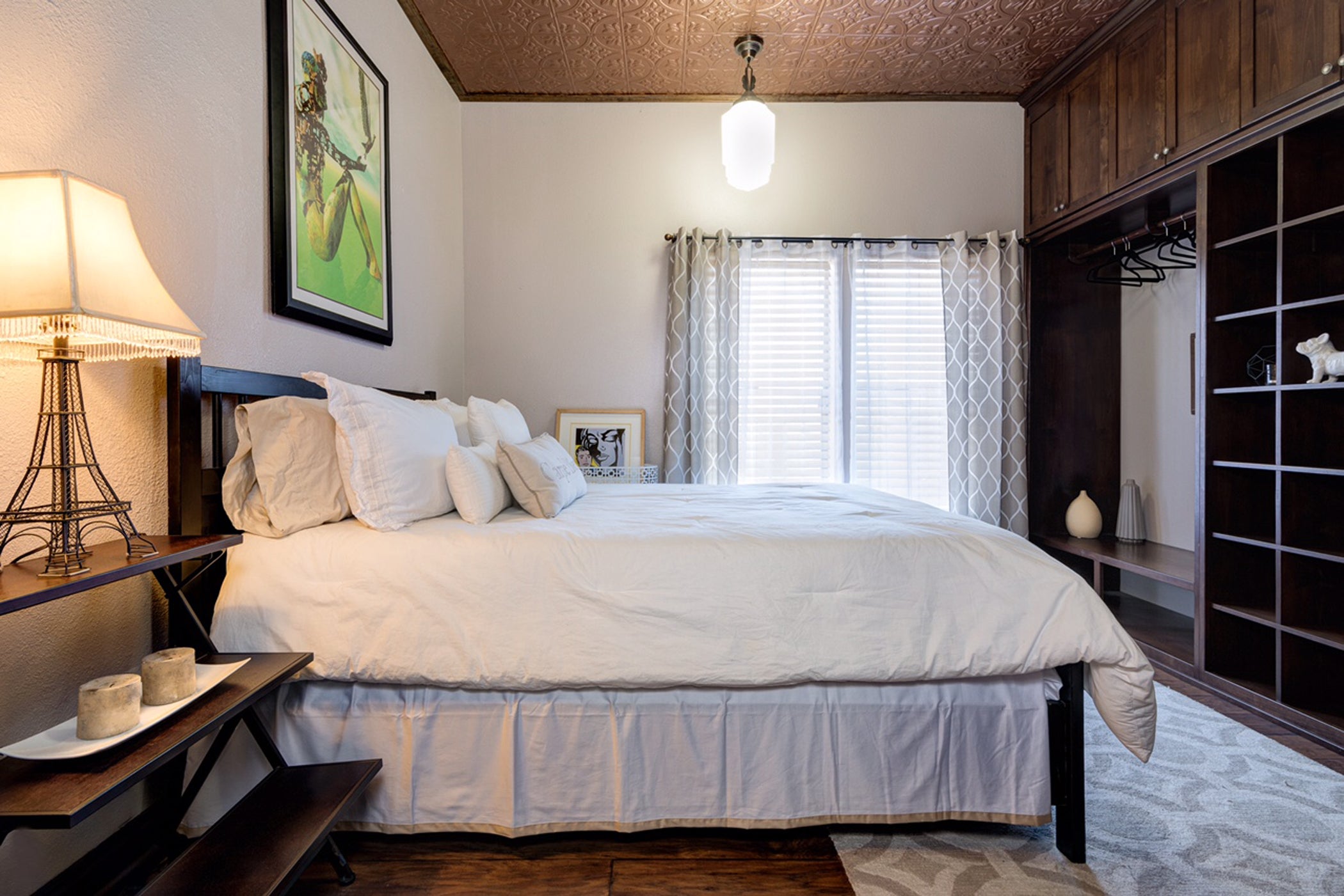 Neatly made bed in a bedroom with a lamp, nightstands, and a window.