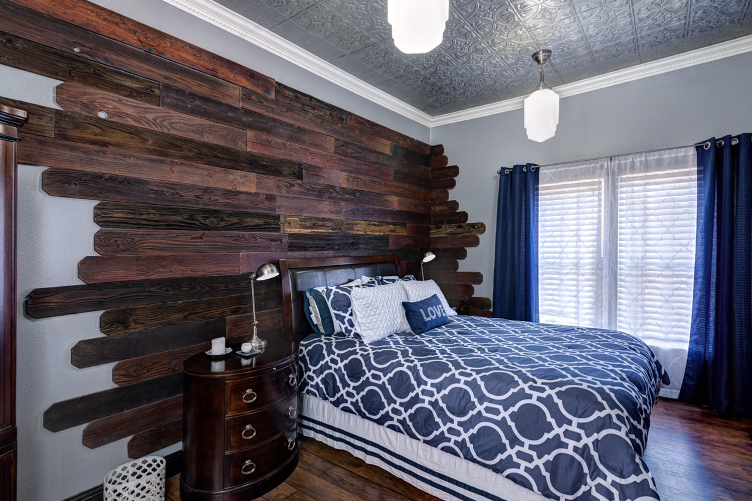 Bedroom with wooden wall paneling, blue and white patterned bedding, and dark wood nightstand.