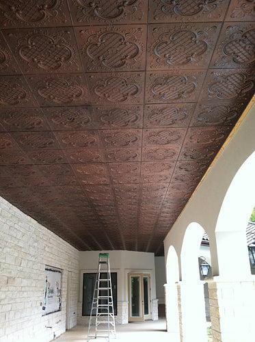 Ceiling with decorative pressed metal tiles in a room with white walls and a ladder.