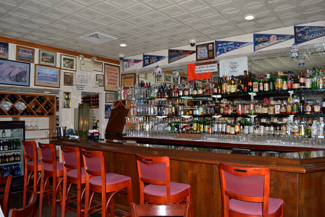 Bar interior with red chairs, shelves stocked with bottles, and various decorations on the walls.