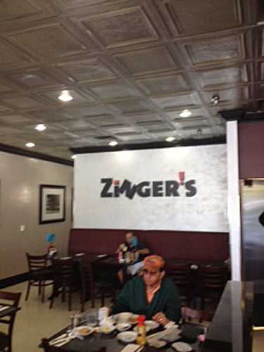 Dining area with 'Zinger's' logo on a screen, people sitting at tables.