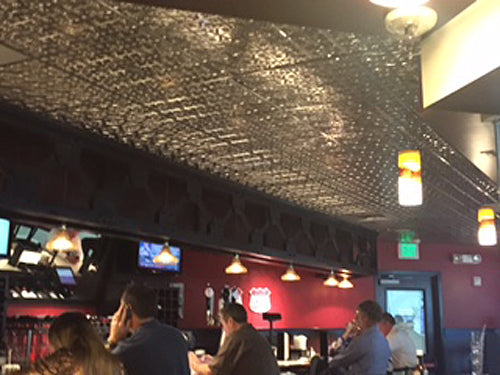 Bar interior with people sitting at tables, ceiling lights, and a red wall.