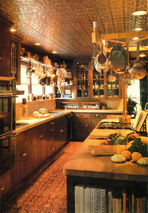 Wooden kitchen with rustic decor, including hanging pots and a variety of vegetables on the counter.