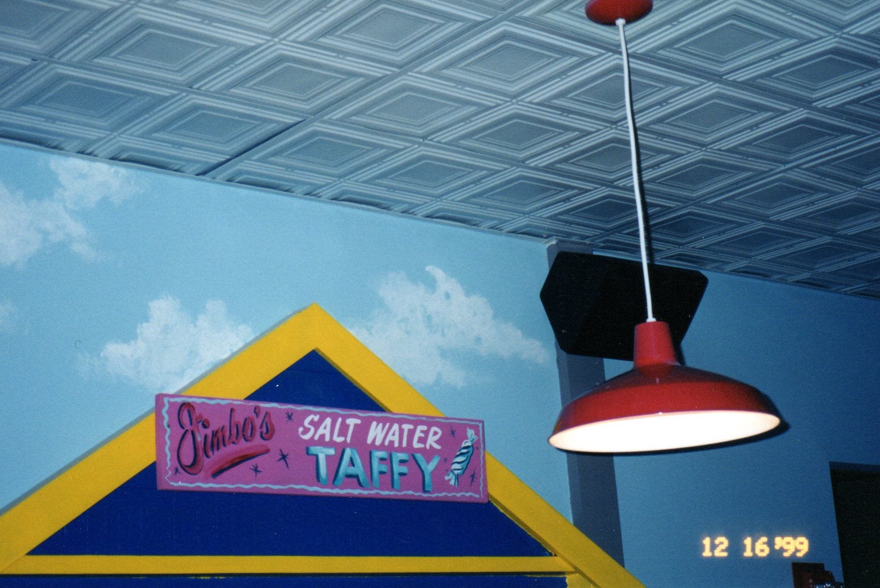 Ceiling with a red light fixture and a sign for 'Simba's Salt Water Taffy' against a blue wall.