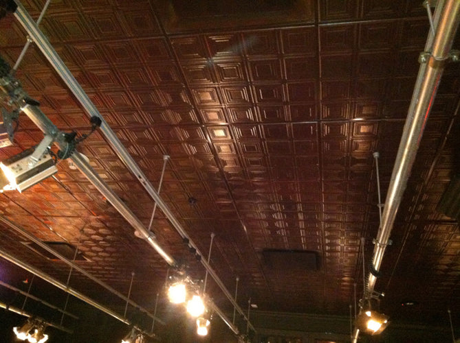 Ceiling with wooden tiles and exposed pipes, featuring light bulbs.