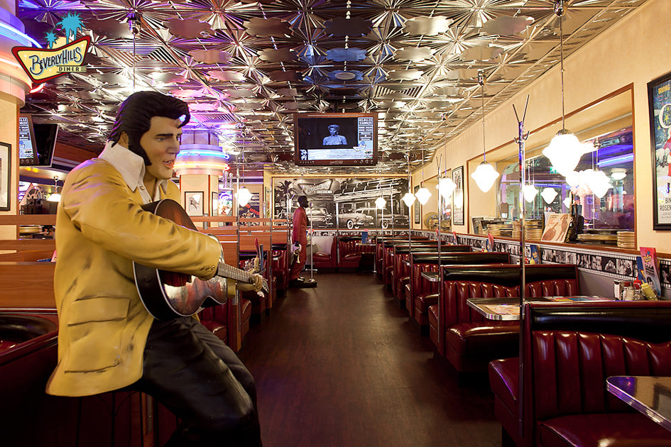 Diner interior with a person in a yellow jacket playing guitar, surrounded by red booths and vintage decor.