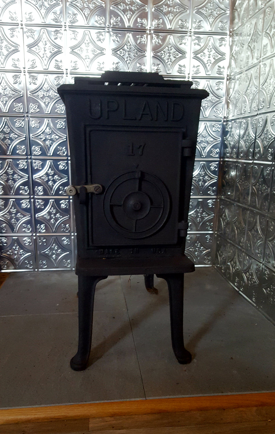 Black cast iron stove with 'Upland' branding against a patterned tiled wall.