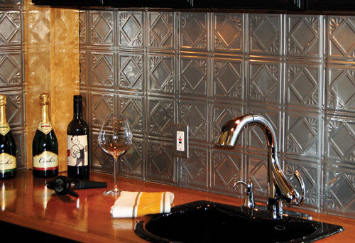 Bottles of wine and a glass on a bar counter with a metallic backsplash.