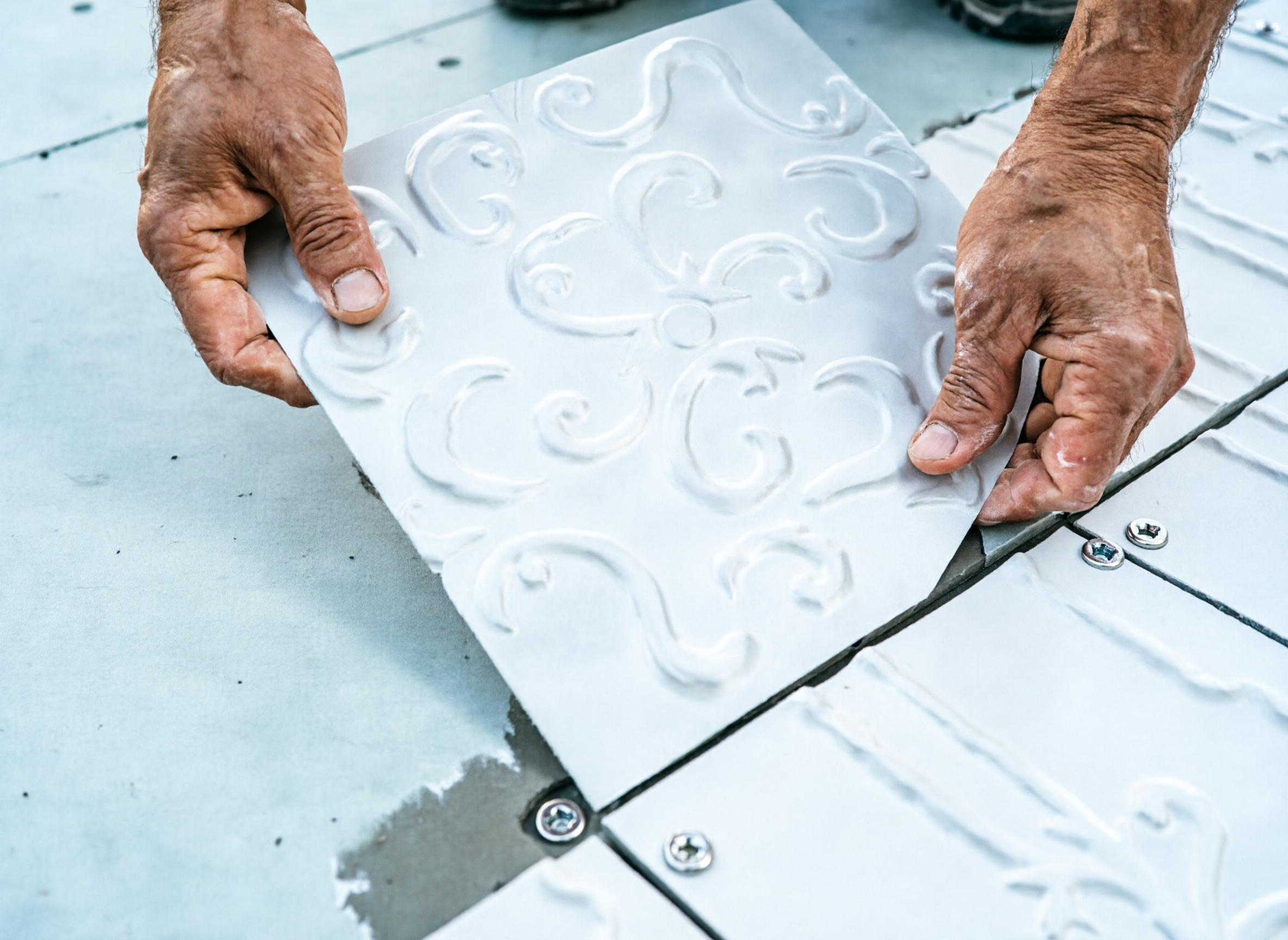 Person applying decorative tile adhesive with a patterned sheet on a tiled floor.