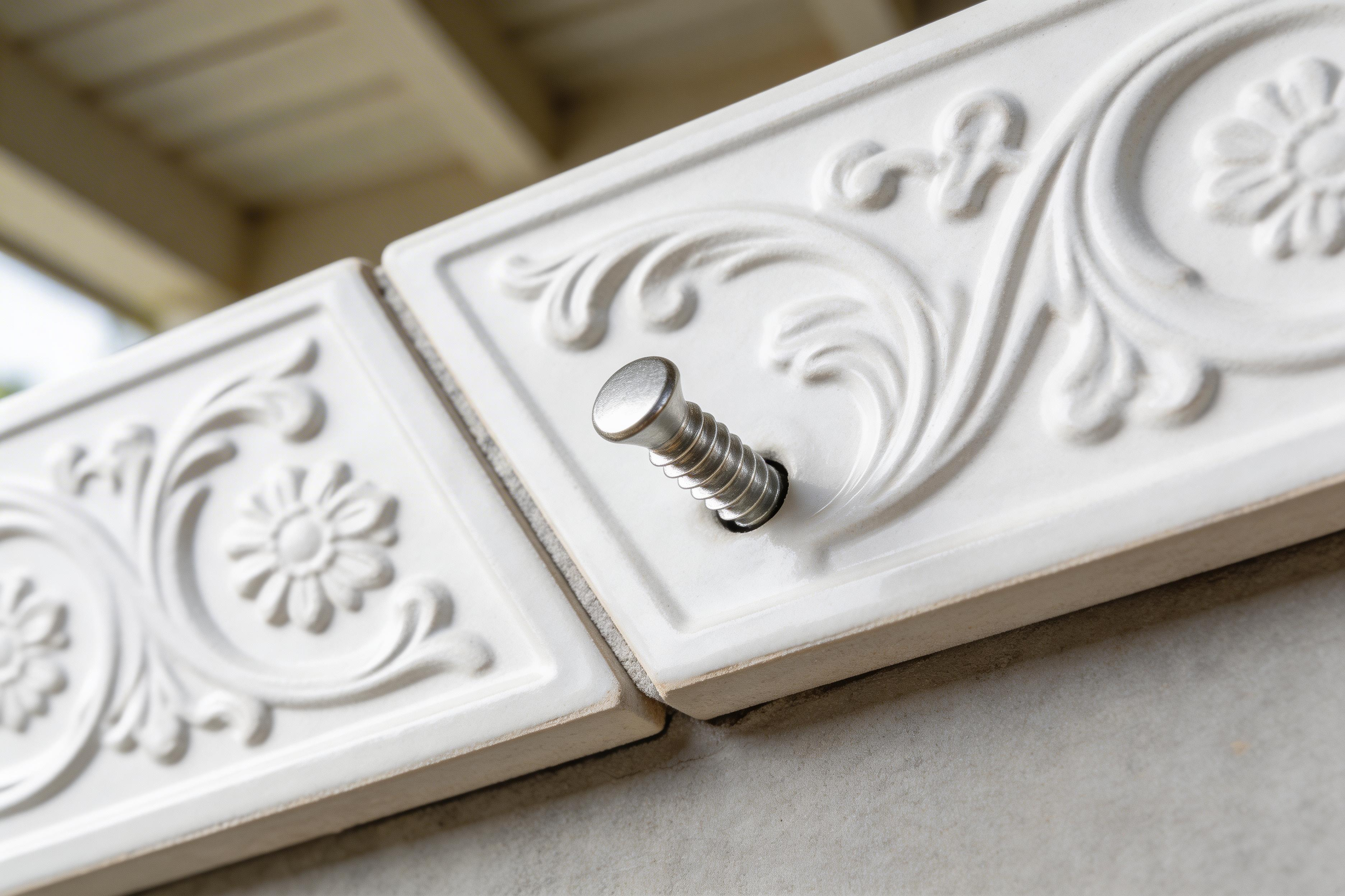 Decorative white tile with intricate patterns and a screw on a neutral background