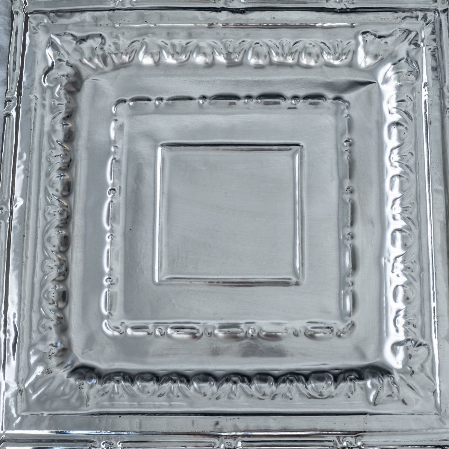 Silver decorative square plate with intricate patterns.