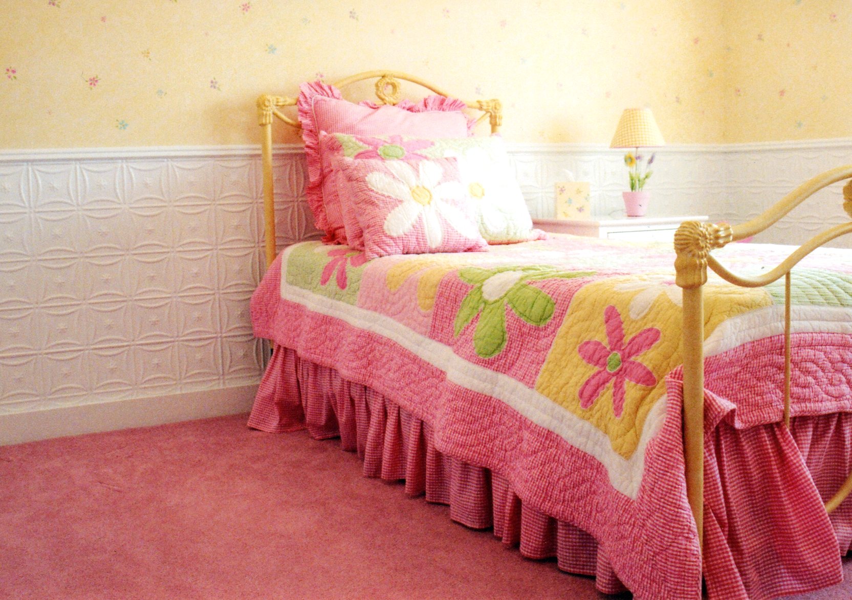 Children's bedroom with a pink bedspread and floral patterns on a yellow bed frame.